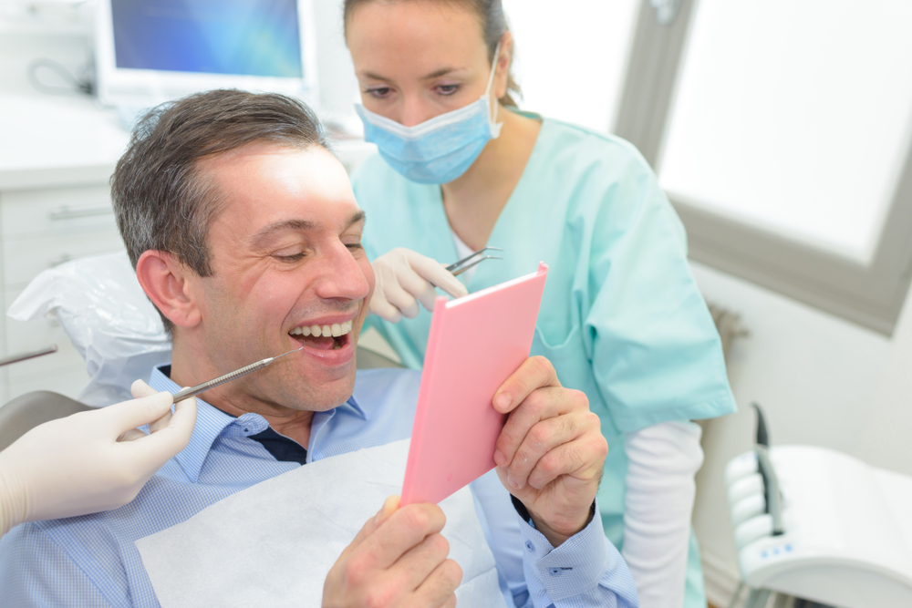 man looking at teeth in mirror at dentist
